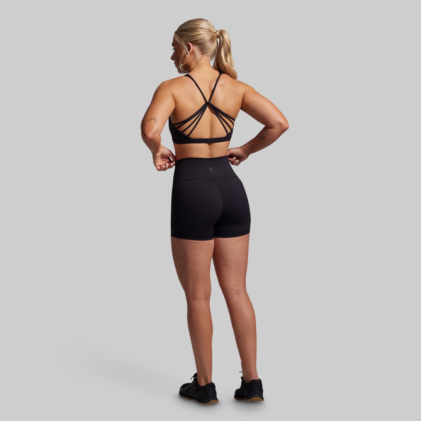 Woman wearing a black sports bra and shorts on a gray background