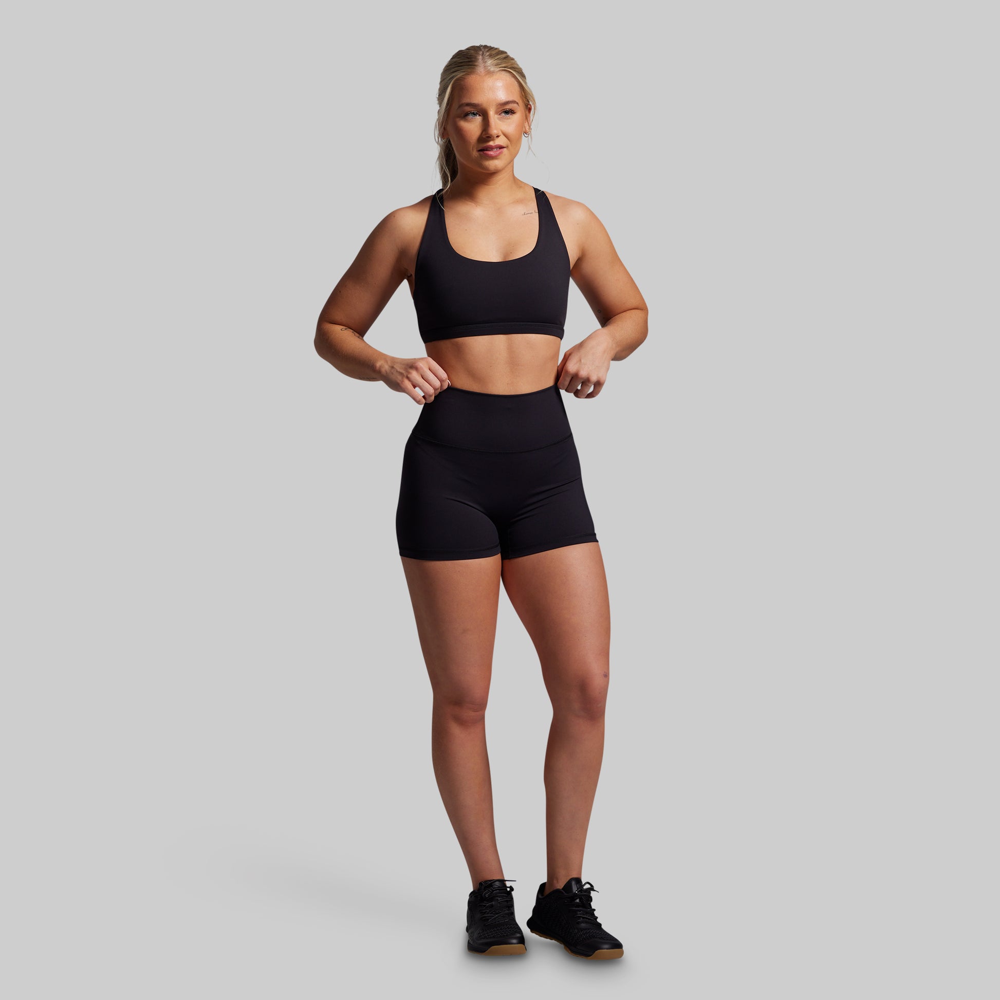 Woman wearing a black sports bra and shorts on a gray background