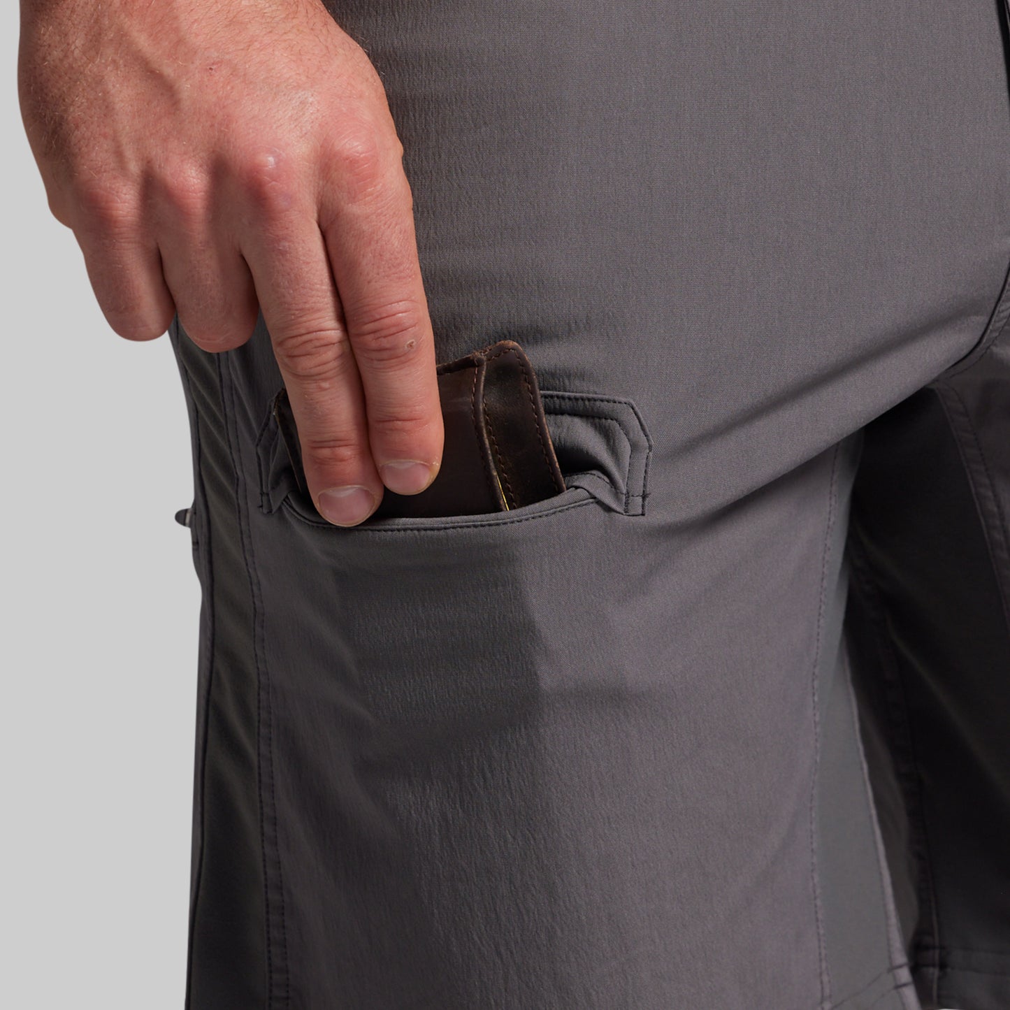 Person inserting a wallet into a pocket of gray shorts on a light gray background