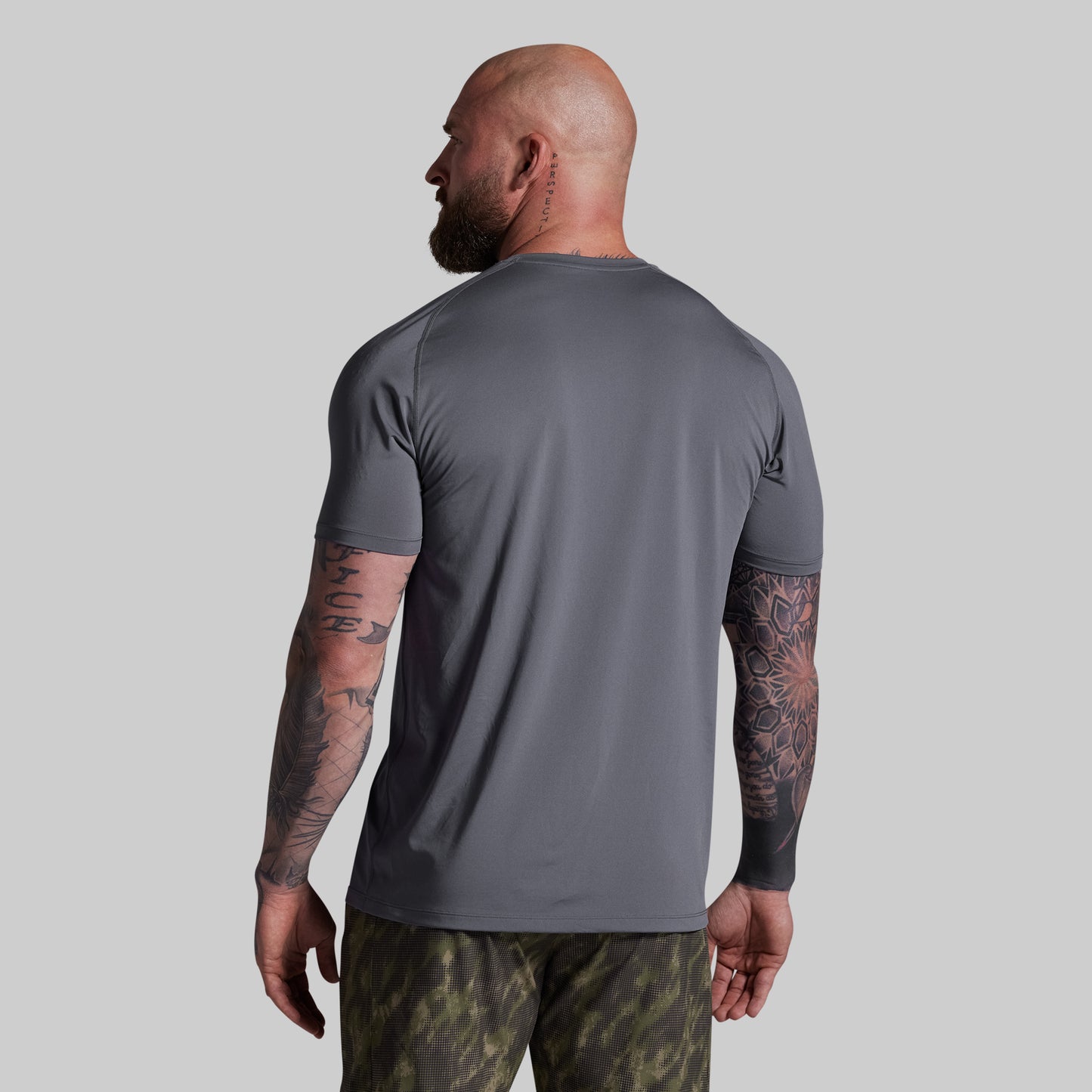 Man wearing a gray t-shirt and camouflage shorts on a plain background