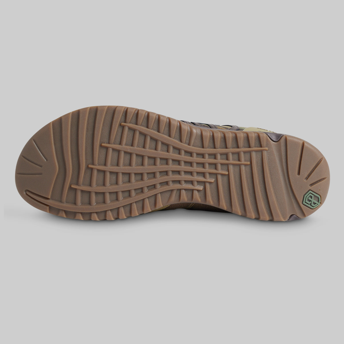 The outsole of a brown hiking boot, showing deep lugs and a small green logo badge on the heel, set against a solid gray background.