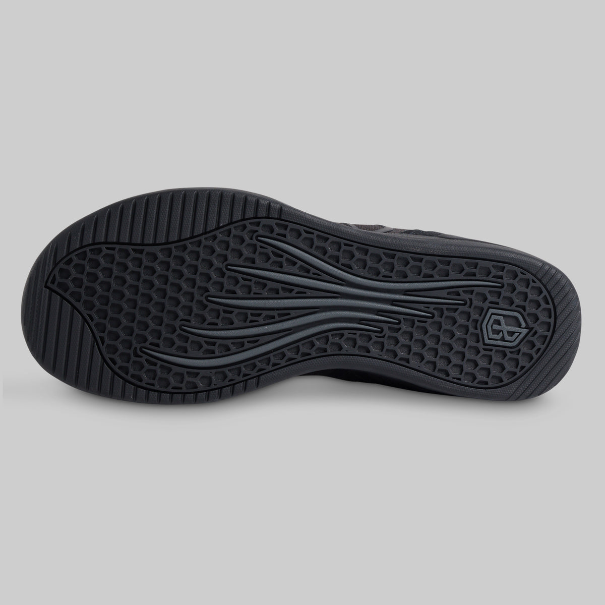 The black rubber outsole of a shoe, showing a textured honeycomb pattern and wavy tread design, photographed from a top-down view on a neutral gray background.
