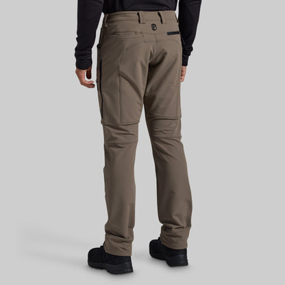 Rear view of a person wearing grey technical cargo pants with black boots and a black long-sleeve top, shown against a light gray studio background.