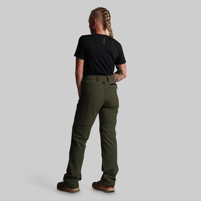 A woman shown from the back wearing olive green cargo-style pants, a black short-sleeve t-shirt, and brown shoes against a plain light gray studio background.