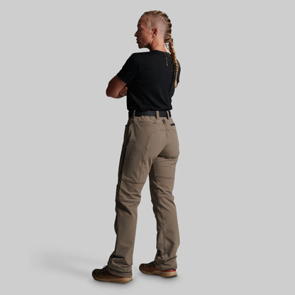 A woman shown from the back wearing grey cargo-style pants, a black short-sleeve top, and brown shoes against a plain light gray studio background.