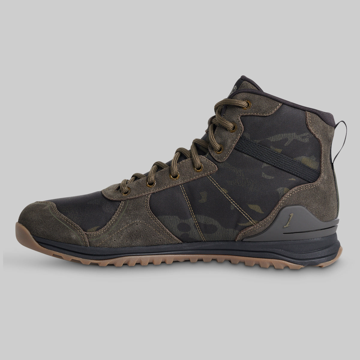 A mid-cut tactical boot in dark camouflage and suede, featuring a black laces system and a rugged brown outsole, shown from a side profile on a light gray background.