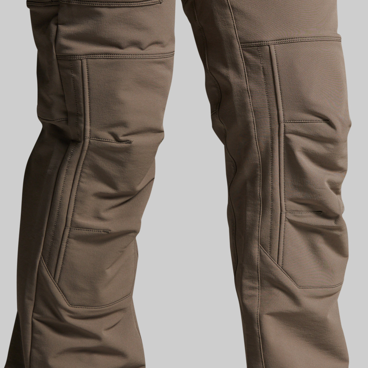 Close-up of a pair of storm grey technical pants showing the knee area with multiple zippered and flap pockets, set against a solid gray background.