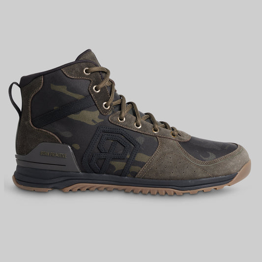 A high-top tactical boot in dark camouflage and suede, featuring a black side logo, metal eyelets, and a rugged brown outsole, shown against a solid gray background.