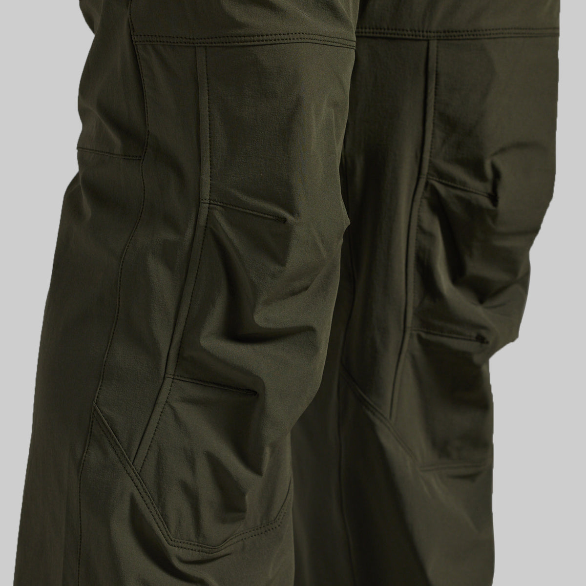 Close-up of dark olive green outdoor pants showing the fabric texture, seams, and side pockets against a neutral gray background.