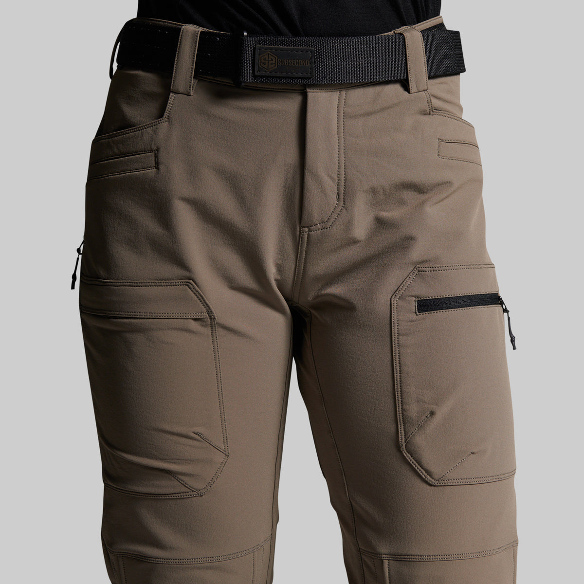 A close-up of a person wearing outdoor cargo pants in a storm grey color, paired with a black belt and black top, against a solid light gray background.