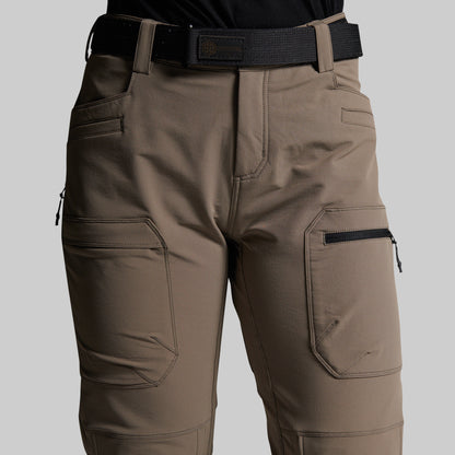 A close-up of a person wearing outdoor cargo pants in a storm grey color, paired with a black belt and black top, against a solid light gray background.