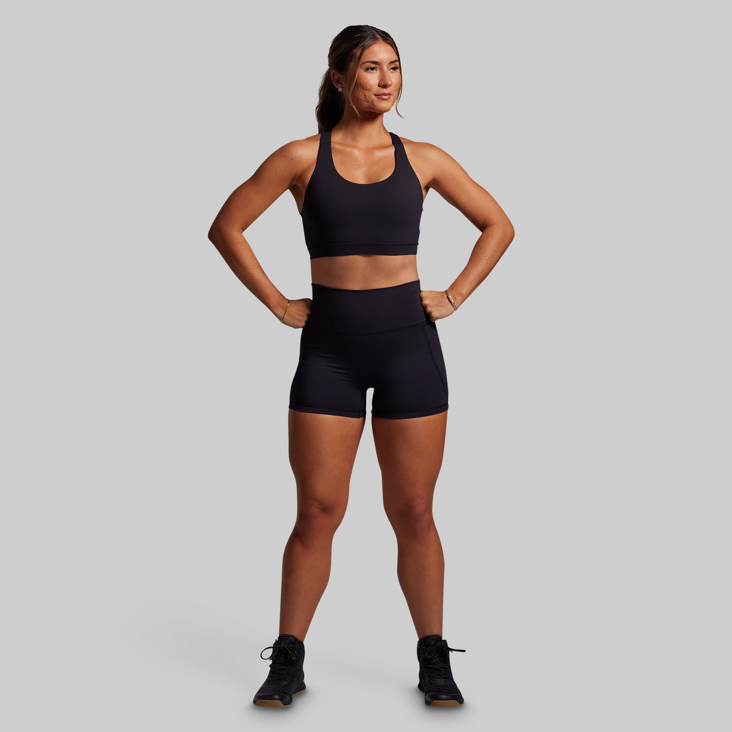 Woman wearing a black sports bra and shorts on a gray background