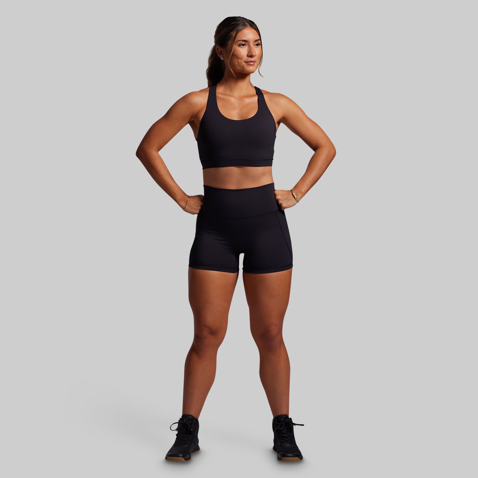 Woman wearing a black sports bra and shorts on a gray background