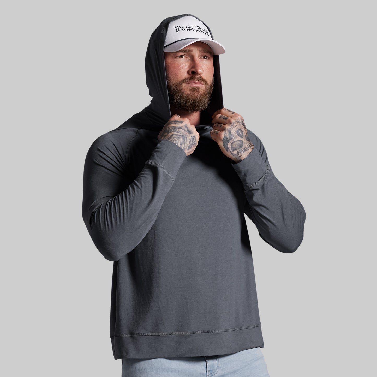 Man wearing a gray hoodie and white cap with text, standing against a plain background