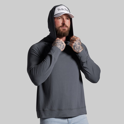 Man wearing a gray hoodie and white cap with text, standing against a plain background