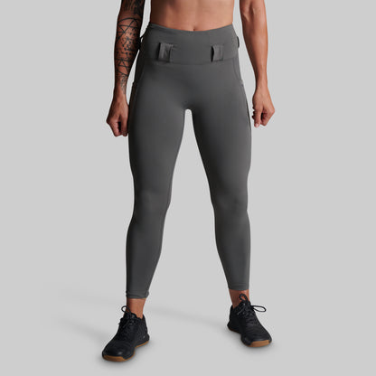 A model from the waist down wearing dark gray high-waisted athletic leggings with belt loops and black athletic shoes, set against a solid light gray background.