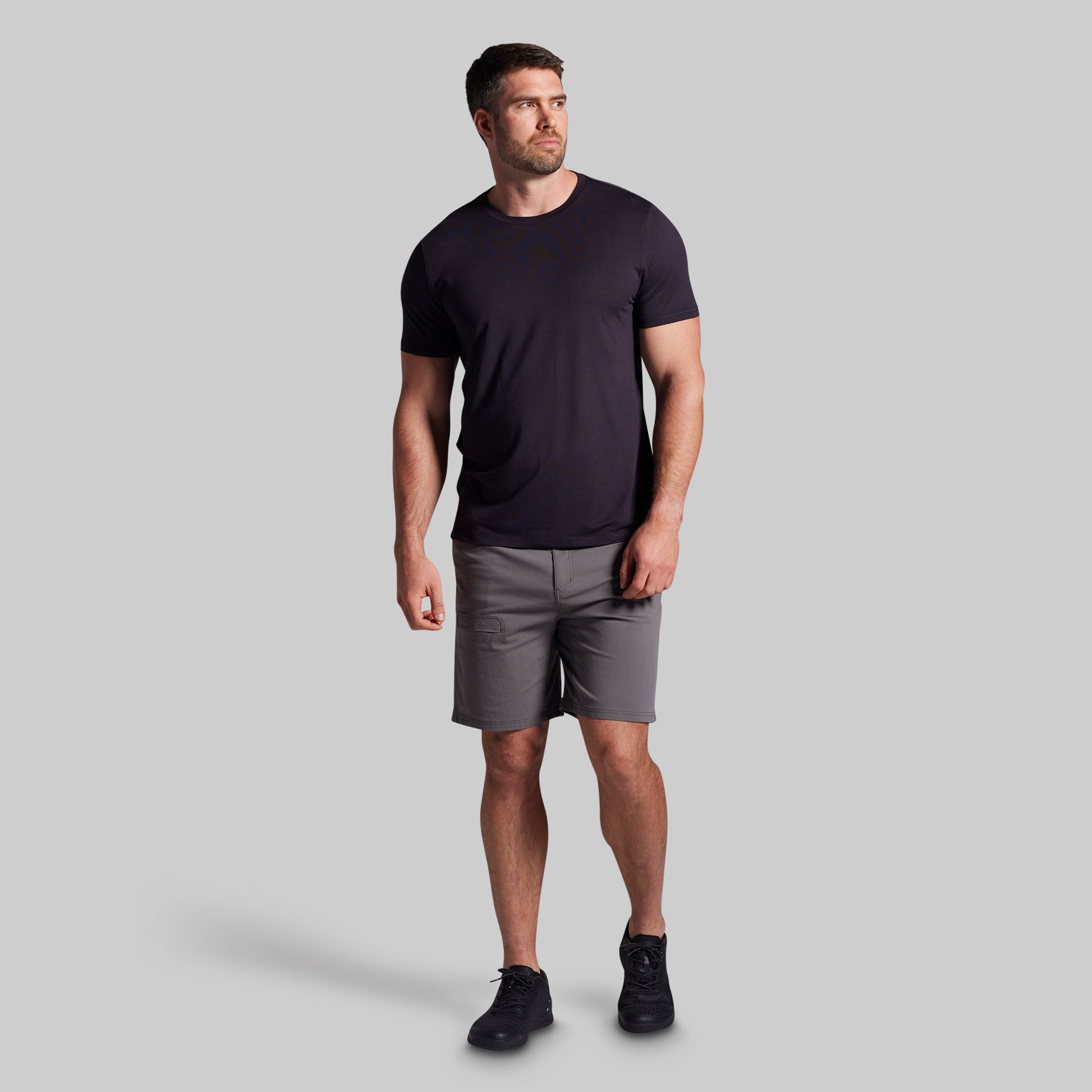 Man wearing a black t-shirt and gray shorts on a light gray background