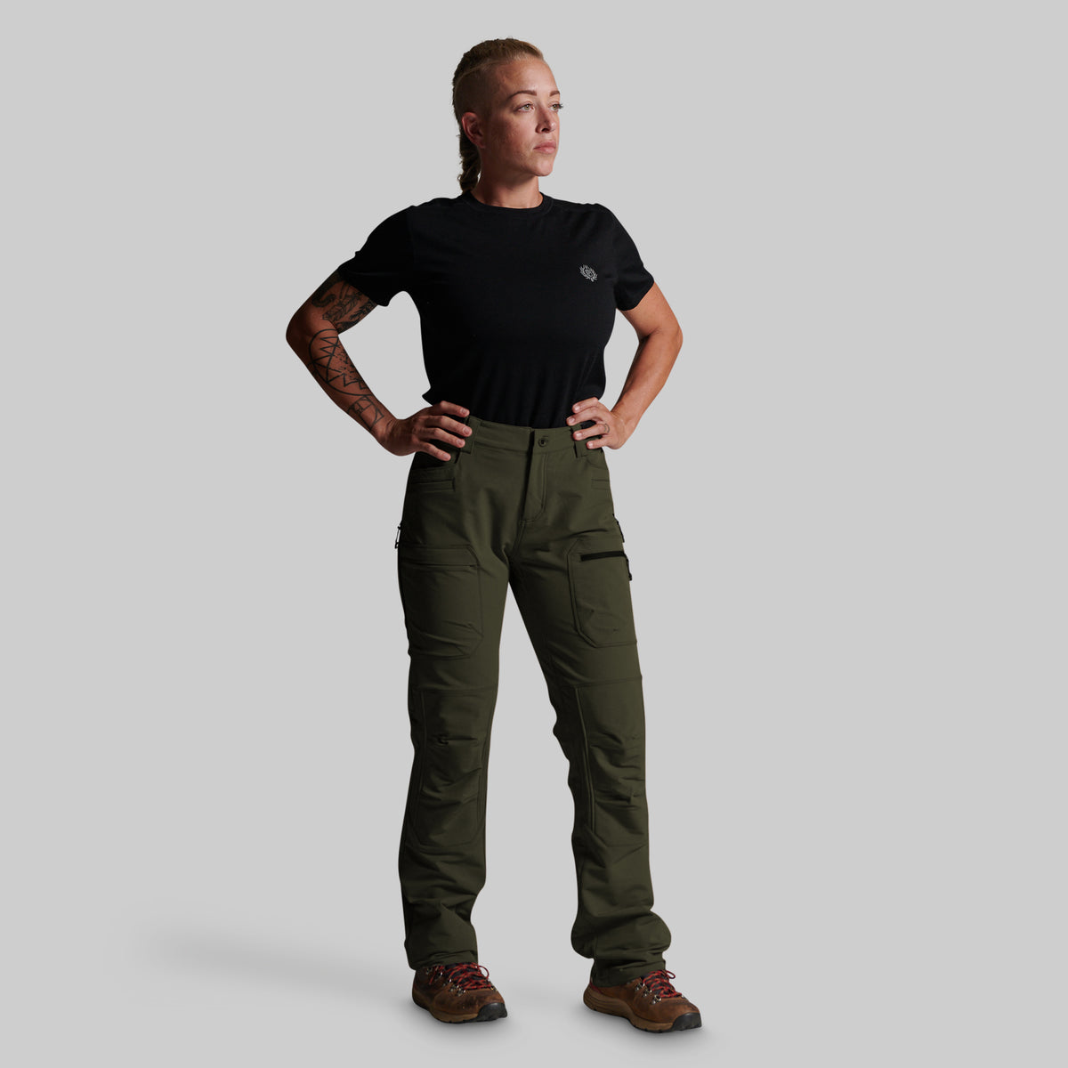 A woman modeling a black short-sleeve t-shirt and olive green cargo pants against a solid light gray background.
