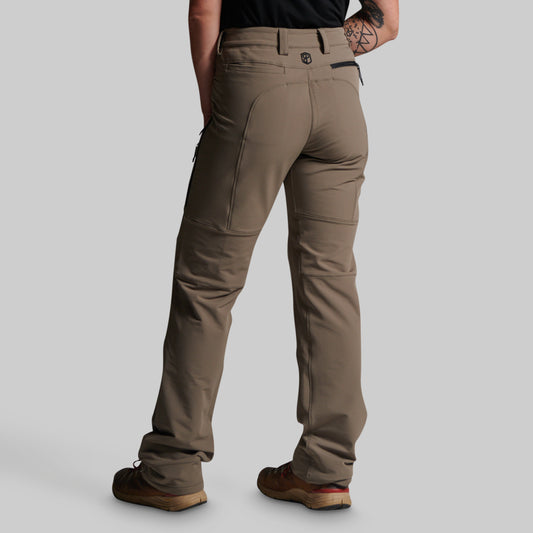 A person shown from the back wearing grey cargo pants, a black shirt, and brown shoes against a light gray studio background.