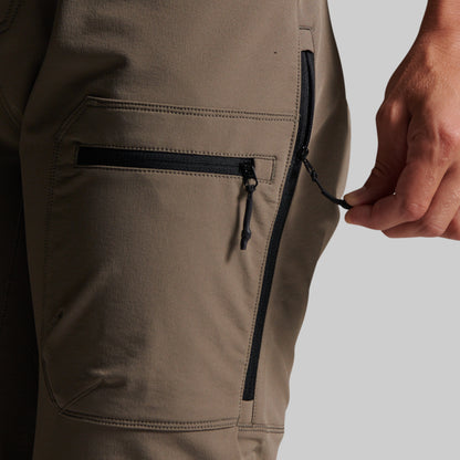 Close-up of grey outdoor pants showing a side zip pocket with a black zipper and a hand pulling the zipper tab.