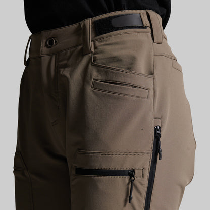 Close-up of a person wearing grey cargo pants with black zippers, belt loops, and a black waistband, shown against a light gray studio background.