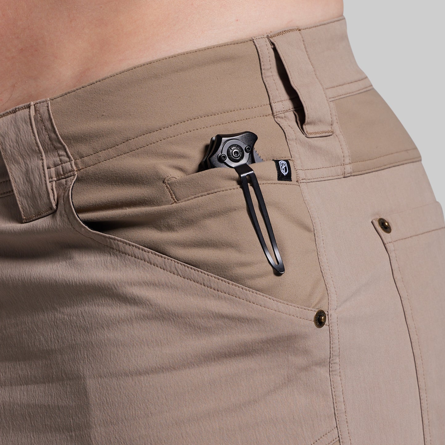 Close-up of beige shorts with a black pocket knife on a neutral background