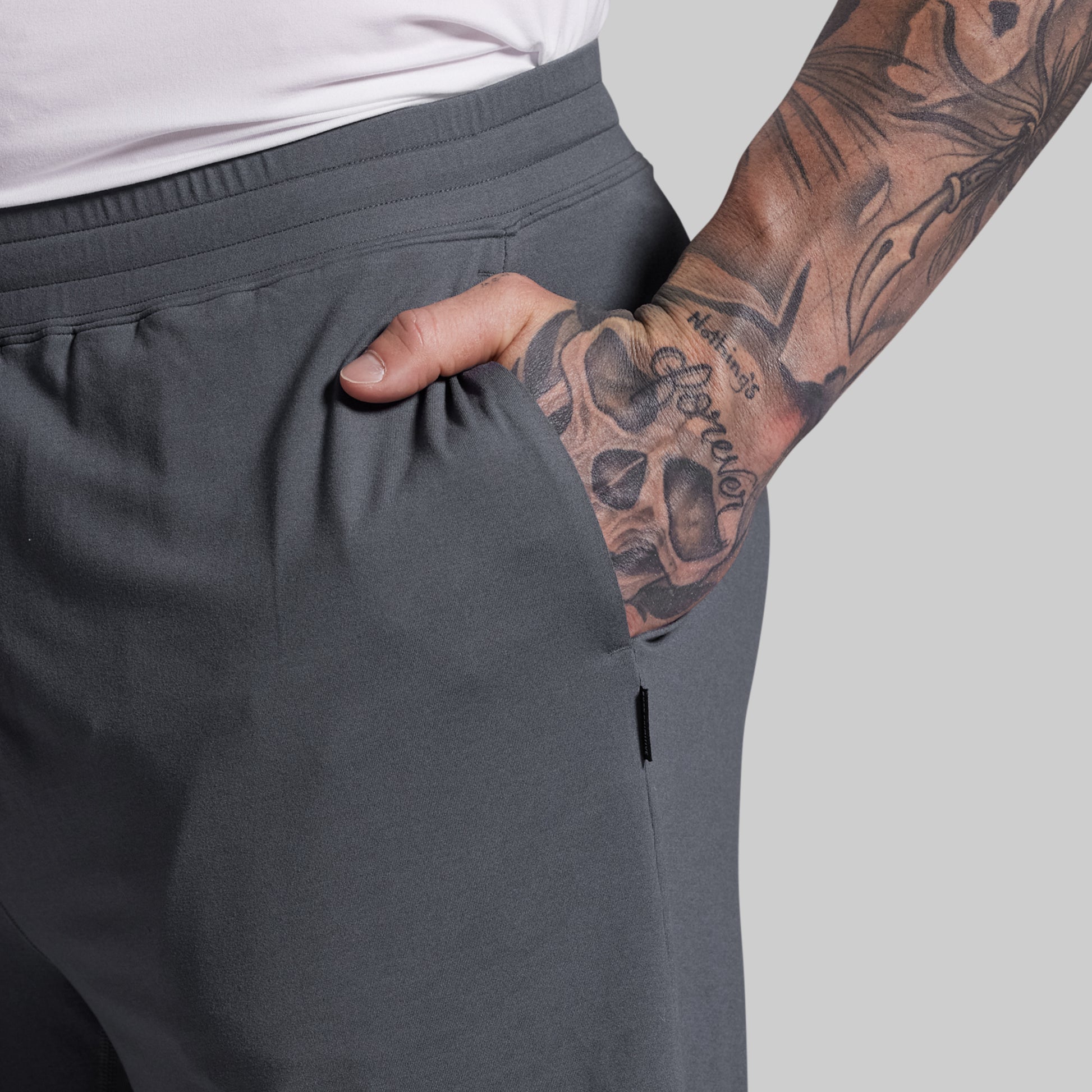 Person wearing gray shorts with a tattooed arm on a light gray background