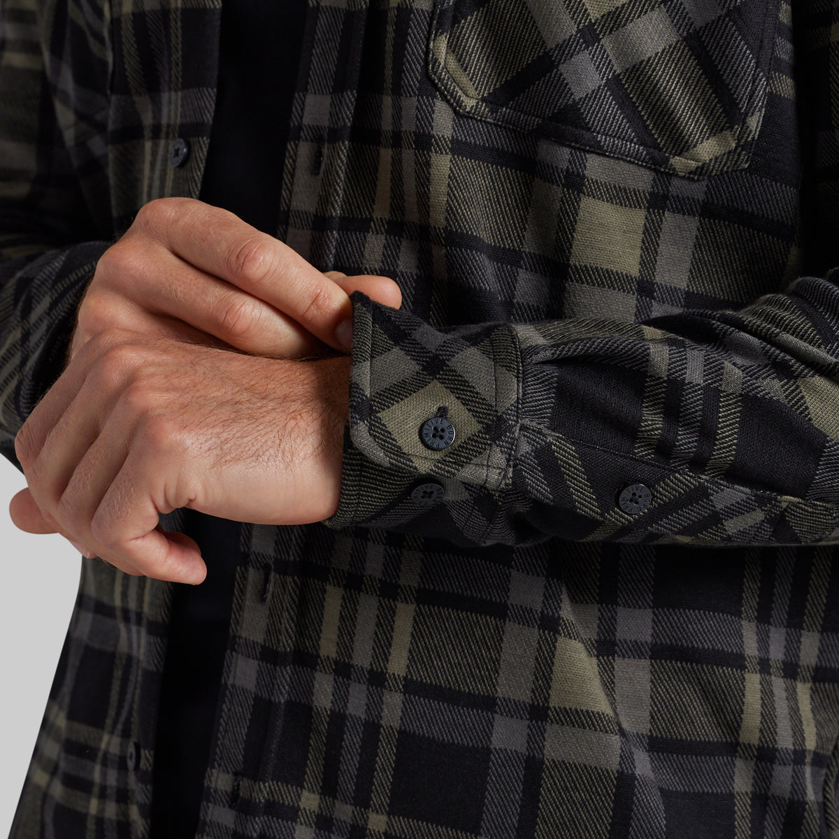 Close-up of a person's hands adjusting the cuff of a dark plaid flannel shirt, showing the fabric texture and button details.