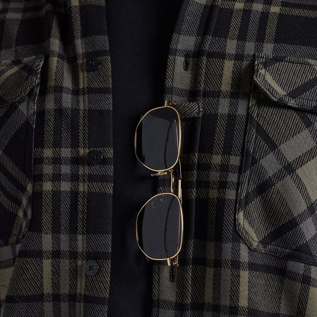 Sunglasses hanging from the placket of a black and gray plaid flannel shirt.