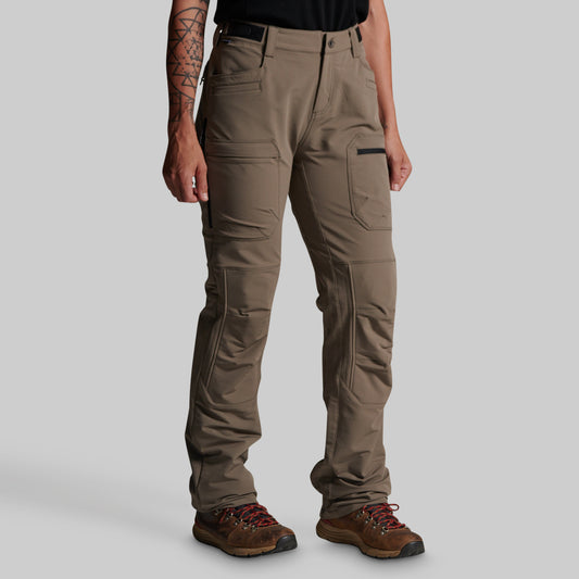 A person wearing grey cargo outdoor pants with a black belt, paired with brown hiking boots, shown from the waist down against a light gray studio background.