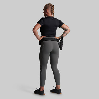 A woman shown from the back wearing dark gray leggings and a black athletic top, with a black tactical belt.