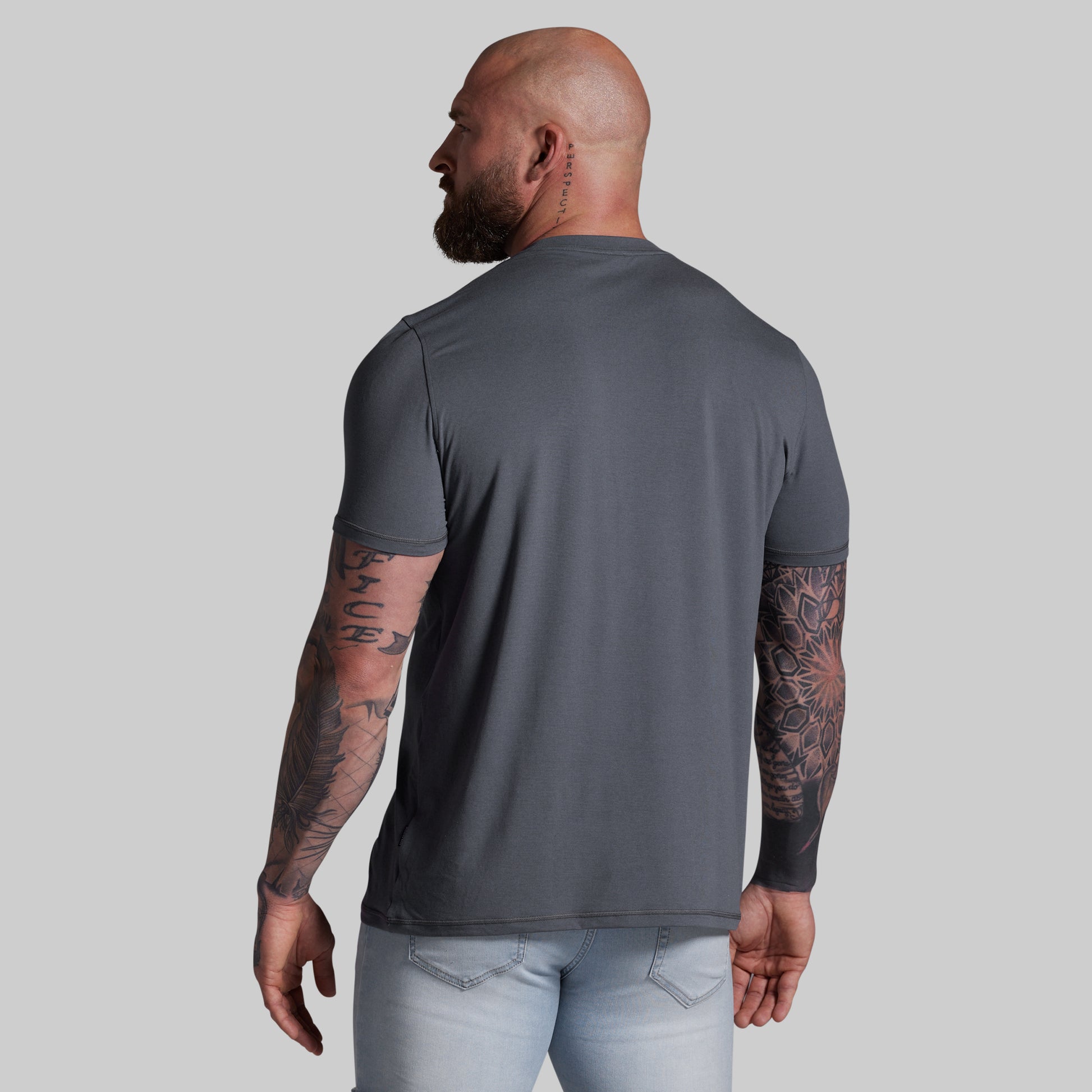 Man wearing a gray t-shirt and light blue jeans against a plain background