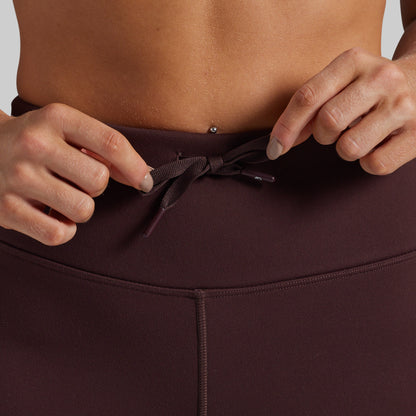 Close-up of a person wearing dark brown high-waisted leggings, adjusting the drawstring waistband.