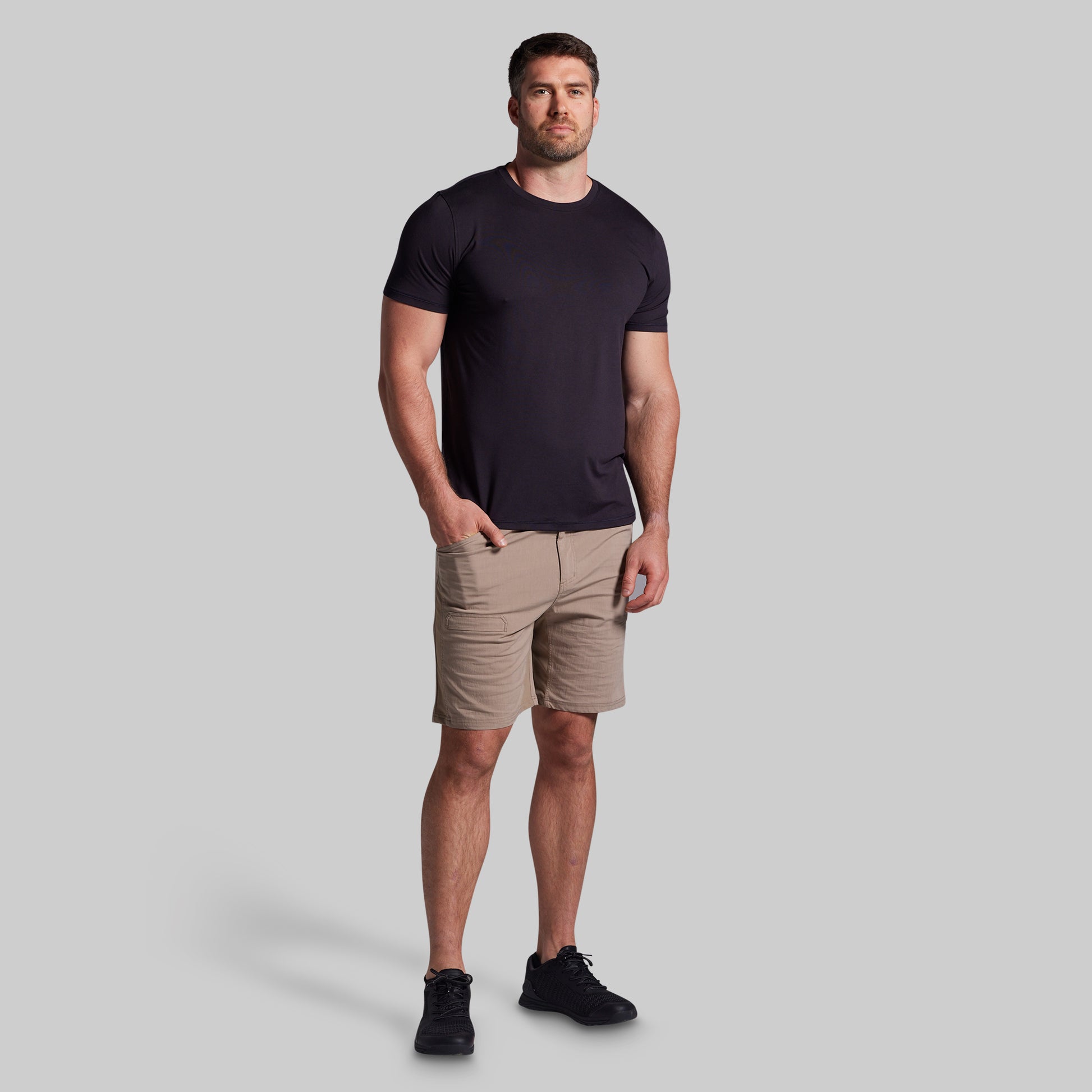 Man wearing a black t-shirt and beige shorts on a gray background