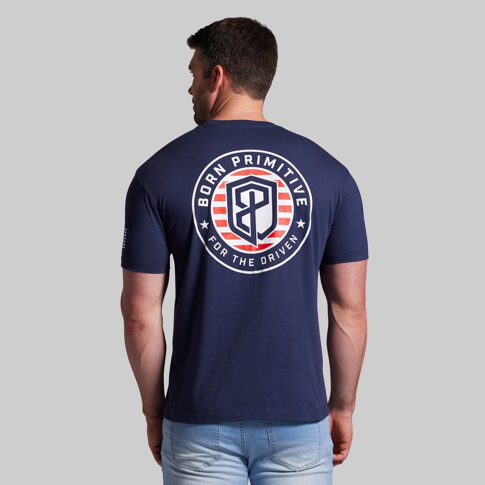 Man wearing a navy blue t-shirt with 'Born Primitive' logo on the back against a gray background