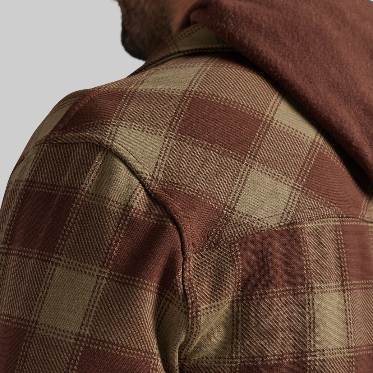 Close-up of a person wearing a brown and tan plaid flannel over a hoodie, showing the shoulder, collar, and hood fabric against a light gray background.