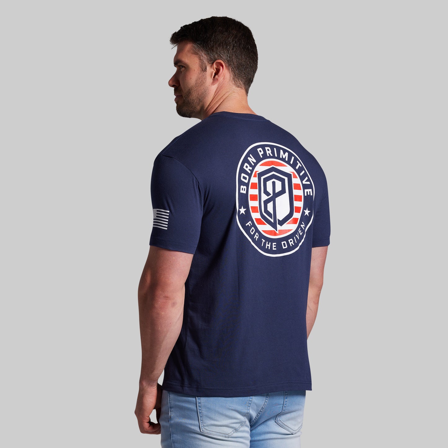 Man wearing a navy blue t-shirt with a logo on the back against a gray background