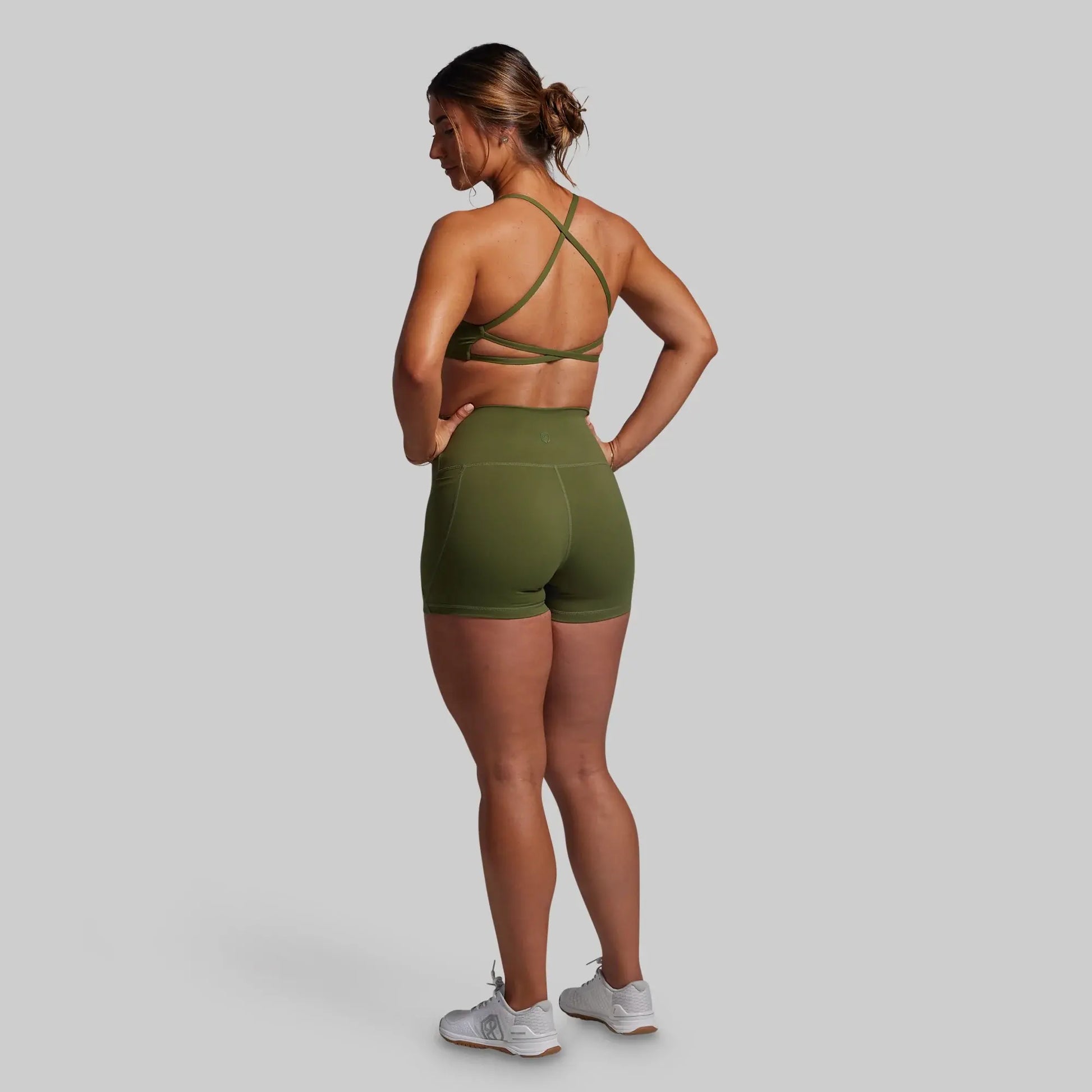 Woman wearing a green sports bra and shorts set on a gray background