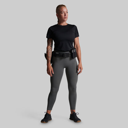 A woman modeling a black short-sleeve tactical shirt and dark gray leggings with a black utility belt and holster, standing against a solid gray background.