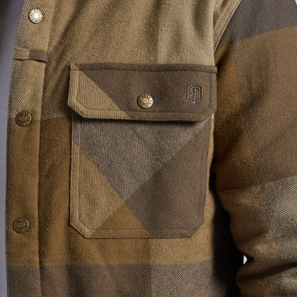 Close-up of a brown and tan plaid flannel jacket showing a chest pocket with a button closure and a small shield logo.