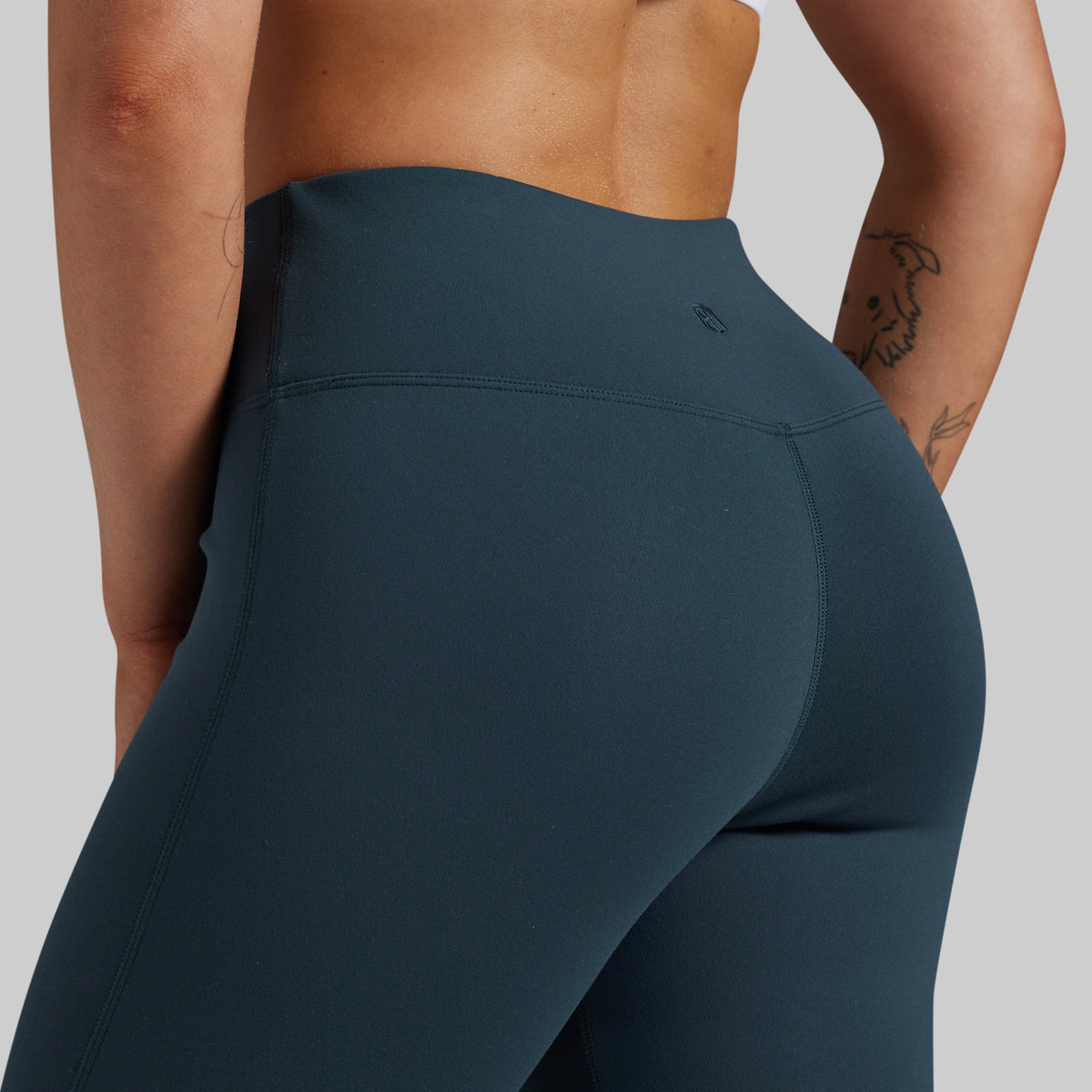 Close-up back view of a model wearing high-waisted dark teal blue-gray leggings against a light gray studio background.