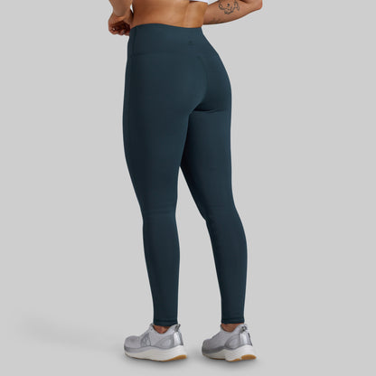 Back view of a model wearing high-waisted dark teal blue-gray leggings against a light gray studio background.