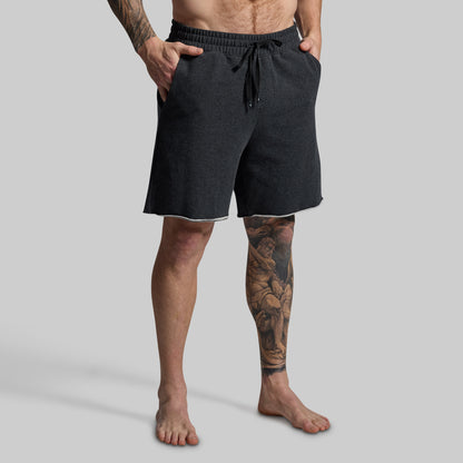 Person wearing dark grey shorts on a gray background