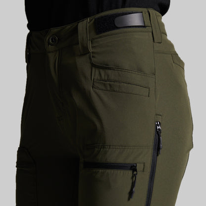 Close-up of olive green cargo pants with multiple zippered pockets and belt loops, shown on a model against a light gray background.