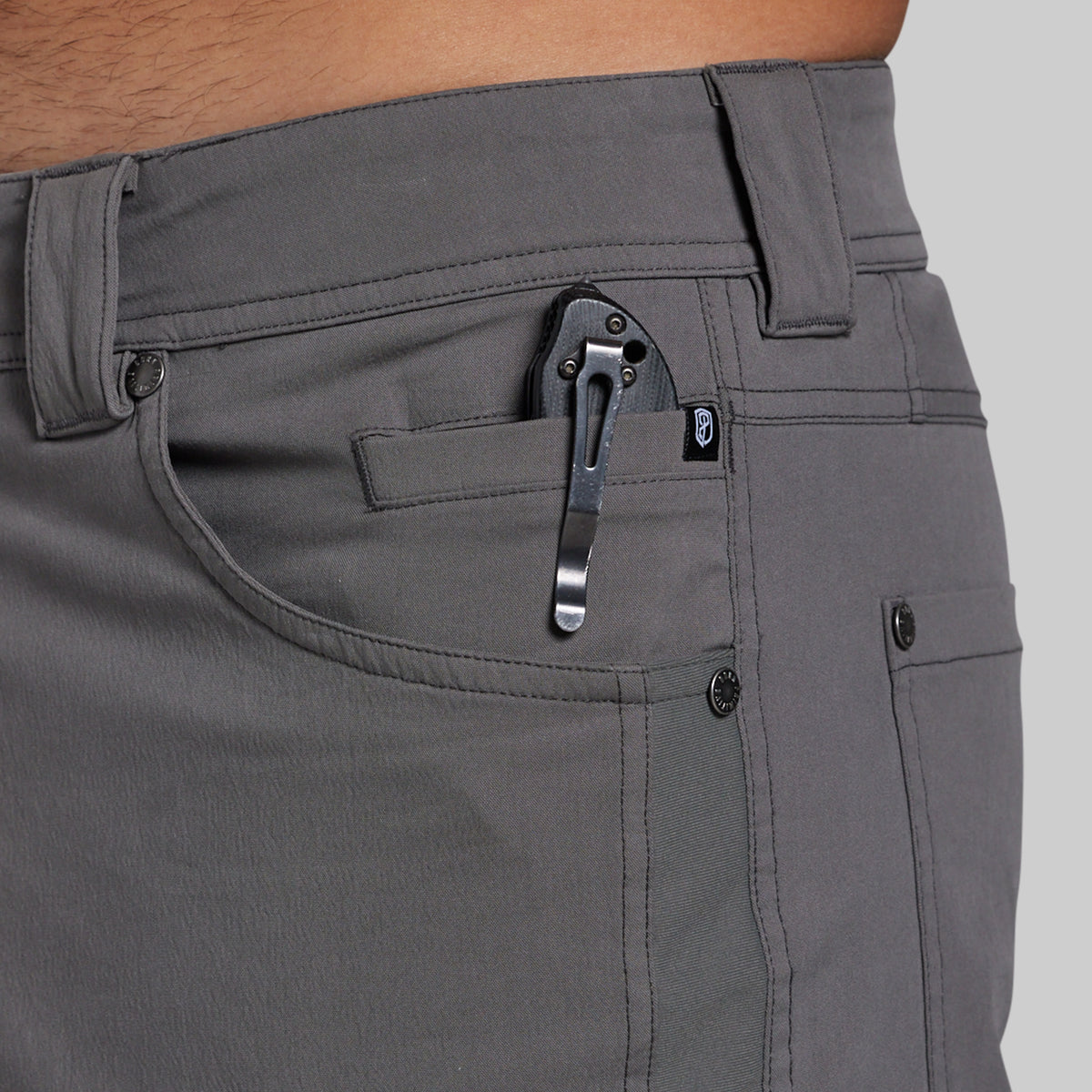 Close-up of a person wearing gray pants, showing the front pocket area with a black knife tucked into the pocket.