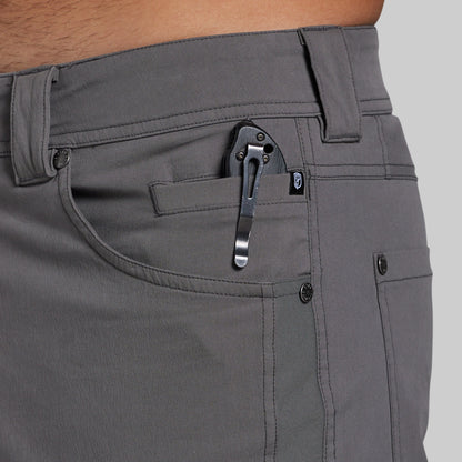 Close-up of a person wearing gray pants, showing the front pocket area with a black knife tucked into the pocket.