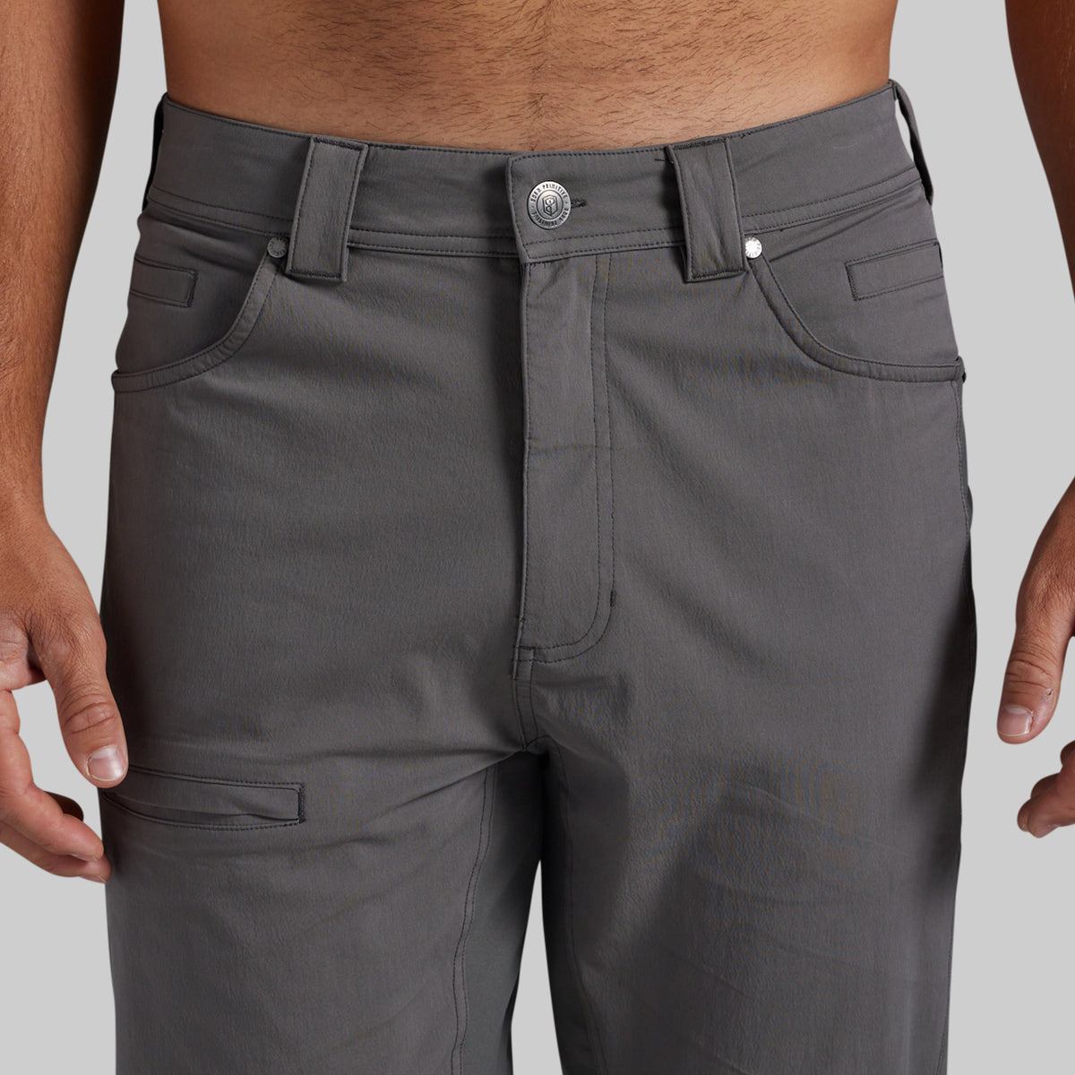 Close-up of a person wearing dark gray cargo-style pants, showing the waistband, front pockets, and upper legs against a light gray studio background.