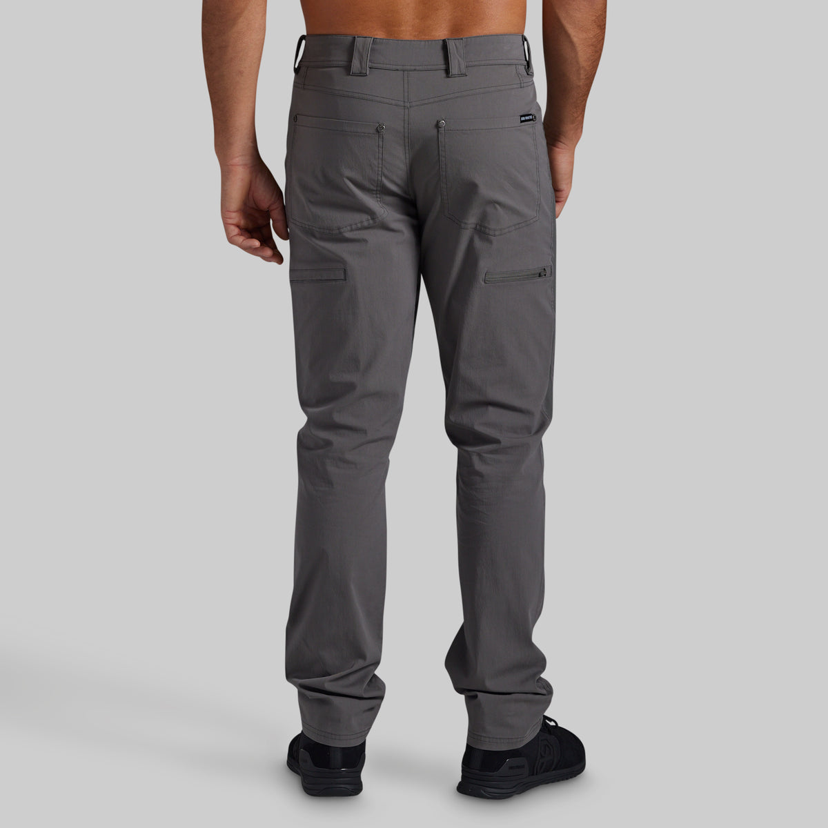 A man shown from the back wearing dark gray cargo pants and black sneakers, photographed against a light gray studio background.