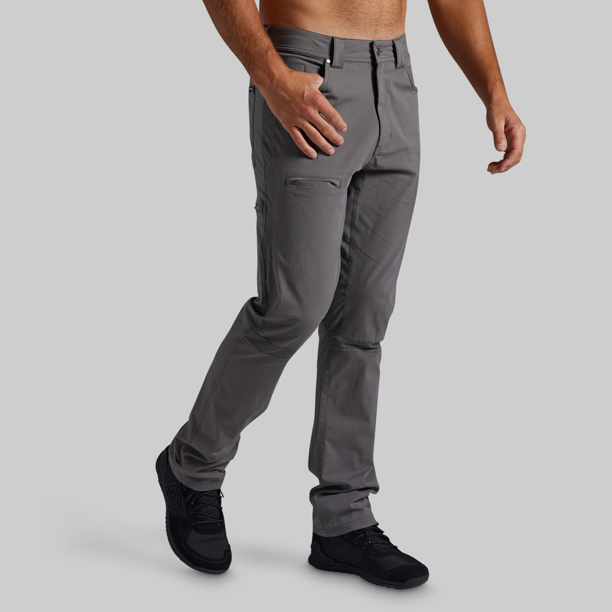 A man wearing gray cargo pants and black shoes, shown from the waist down against a solid gray background.