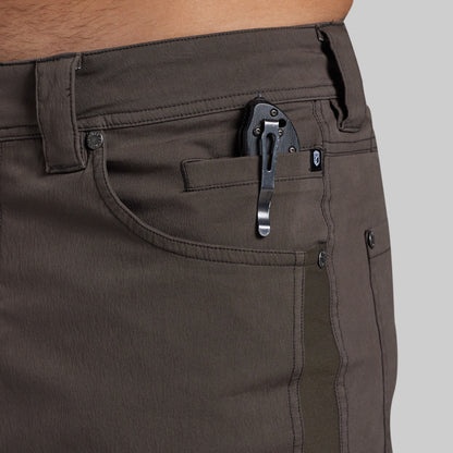 Close-up of a person wearing dark olive brown pants, showing the side pocket with a black metal clip holding a folding knife.